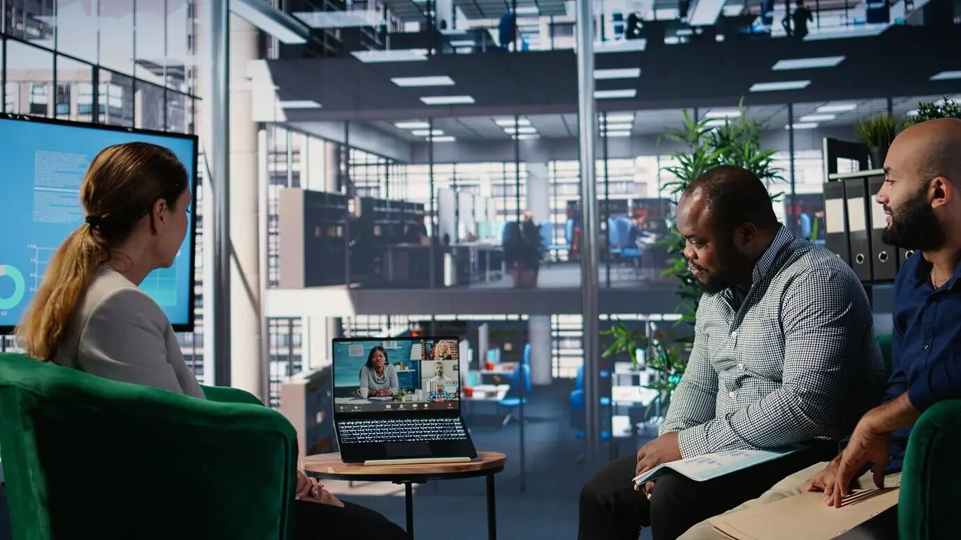 Бизнес-лидеры разных национальностей участвуют в веб-видеоконференции в холле офиса, обмениваясь стратегией.